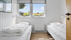 Ein kleiner, heller Raum mit zwei Einzelbetten, einem Heizkörper und einem Fenster mit Blick auf ein Gebäude und Bäume.
