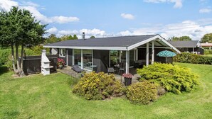 Ein modernes Haus mit überdachter Terrasse, Schornstein und gepflegtem Garten.