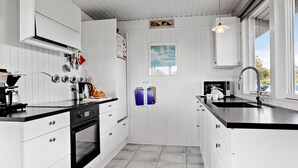 Eine moderne Küche mit weißen Schränken, einer schwarzen Arbeitsplatte und einem eingebauten Backofen. Ein Fenster sorgt für natürliches Licht und bietet einen Ausblick nach draußen.