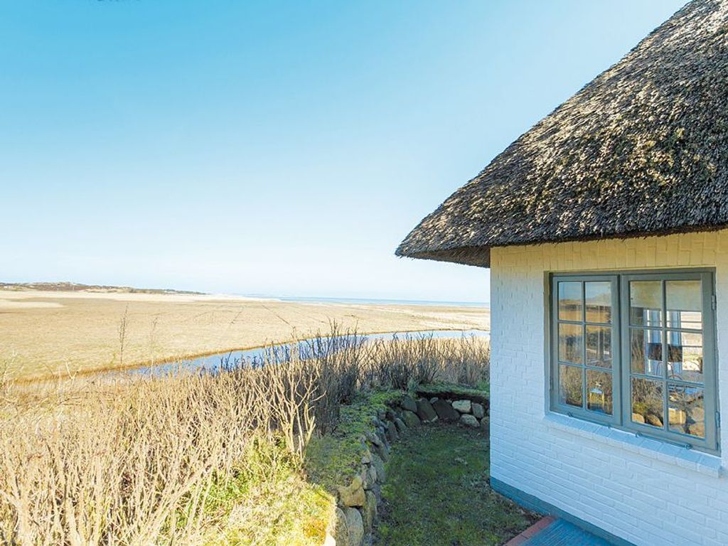 A house with a thatched roof, a stone wall, and a view of a water body.