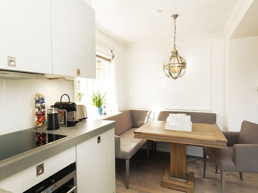 Une cuisine moderne avec des meubles blancs, un four encastré et un coin repas comprenant une table et des chaises en bois.