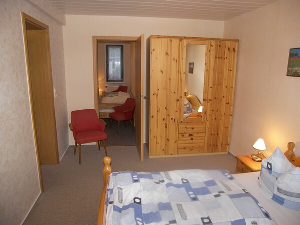A bedroom with a bed, a red chair, a wooden wardrobe, and a desk with a chair.