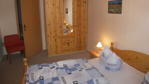 Ein Schlafzimmer mit einem Holzschrank, einem roten Sessel, einer Nachttischlampe und einem Bett mit gemustertem Überwurf.