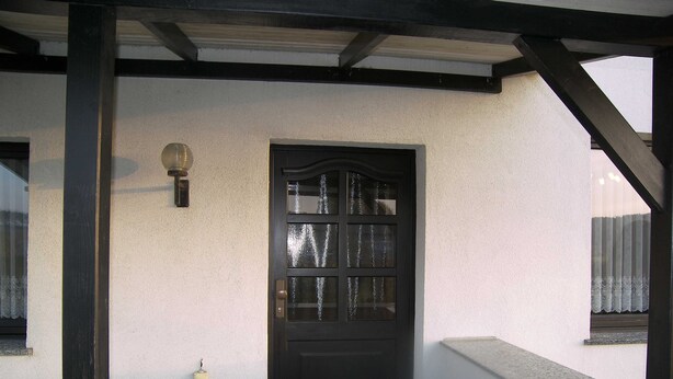 Eine schwarze Tür mit Glasfenster, eine Wandleuchte und eine kleine Stromdosenleiste an einer strukturierten Wand.