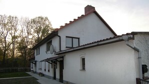 Ein zweistöckiges Haus mit weißer Fassade, einem Ziegeldach und einer kleinen Veranda mit Topfpflanzen.