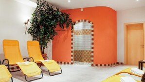 Une pièce aux murs orange, avec une arche ornée de carreaux et une plante en pot. On y trouve des chaises jaunes et une table sur laquelle sont posées des serviettes.