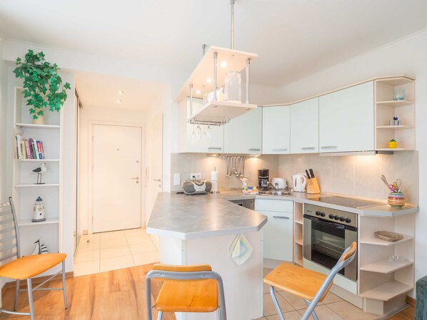 A modern kitchen with white cabinets, a central island with stools, a built-in oven, and a hanging light fixture.