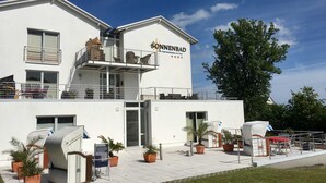 Un hotel moderno con facciata bianca, un balcone con mobili in vimini e piante in vaso.
