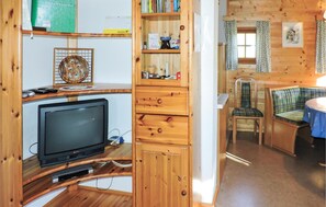 Ein gemütliches Blockhaus-Interieur mit Holzvertäfelung, einem Fernseher, einem Bücherregal und einem Essbereich mit Stuhl und Tisch.