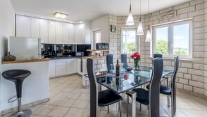 Een moderne keuken met witte kasten, een eethoek met een glazen tafel en zwarte stoelen, en een stenen muur met een raam.