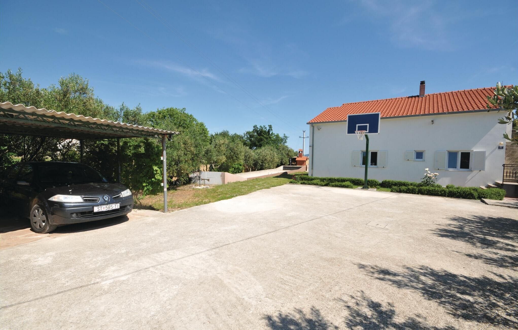 A residential area with a car parked under a covered parking area, a basketball court, and a house with a red-tiled roof.
