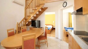 Eine kompakte Küche mit einer Holztreppe, ein Essbereich mit Stühlen, ein Fernseher und ein Bett im angrenzenden Zimmer.