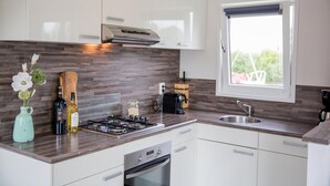 A modern kitchen with white cabinets, a wooden backsplash, a gas stove, a built-in oven, and a window with a view of greenery outside. - Awesome home in Breukelen (Breukelen)