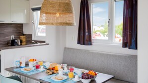 A modern kitchen with a dining table set for breakfast, featuring a wicker pendant light, a view of the outdoors through a window, and a bench seating area. - Awesome home in Breukelen (Breukelen)