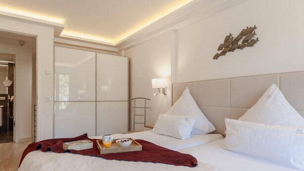A hotel room with a bed, a bedside table with a tray of breakfast, a wall-mounted lamp, and a door leading to another room.