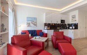 Um espaço compacto com cozinha compacta, um sofá de couro vermelho, um quadro na parede e uma estante com livros e objetos decorativos.