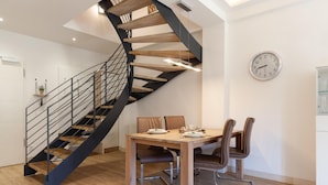 A modern kitchen with a spiral staircase, a dining table with chairs, and a wall clock.