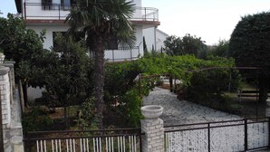 Ein zweistöckiges Haus mit Balkon, umgeben von einem Garten mit verschiedenen Pflanzen und einem Kiesweg.