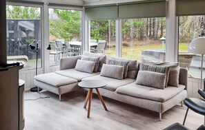A modern living room with a sectional sofa, a round coffee table, and large windows offering a view of the outdoors. - Nice home in Jerup with sauna (Jerup)