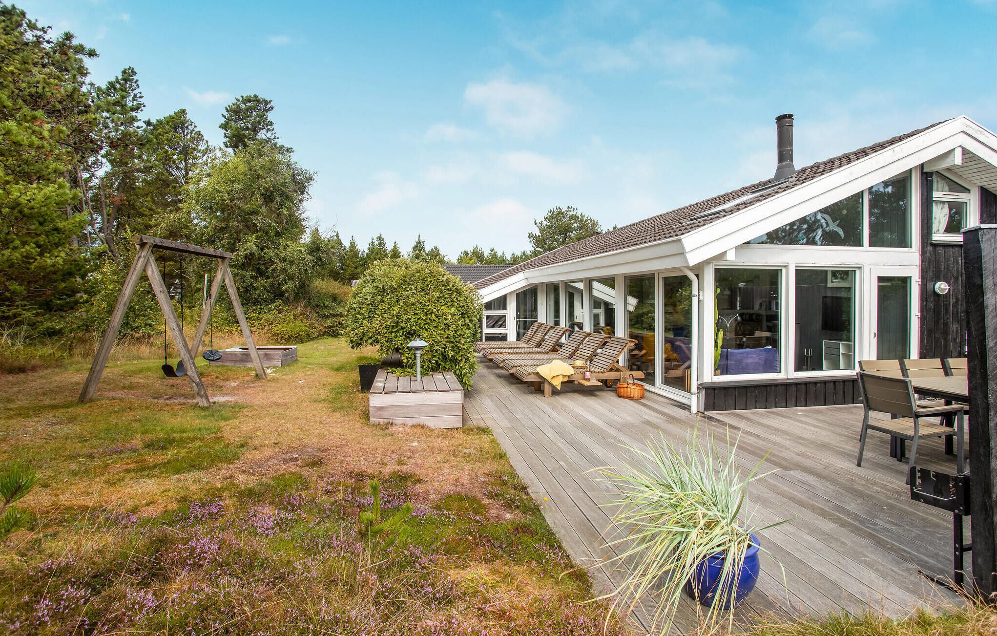 A modern house with a wooden deck, outdoor seating, and a swing set.