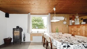 A cozy room with a wooden ceiling, a large window, a dining table with chairs, a stove, and a clock on the wall. - Pet friendly home in Rømø with sauna (Rømø)