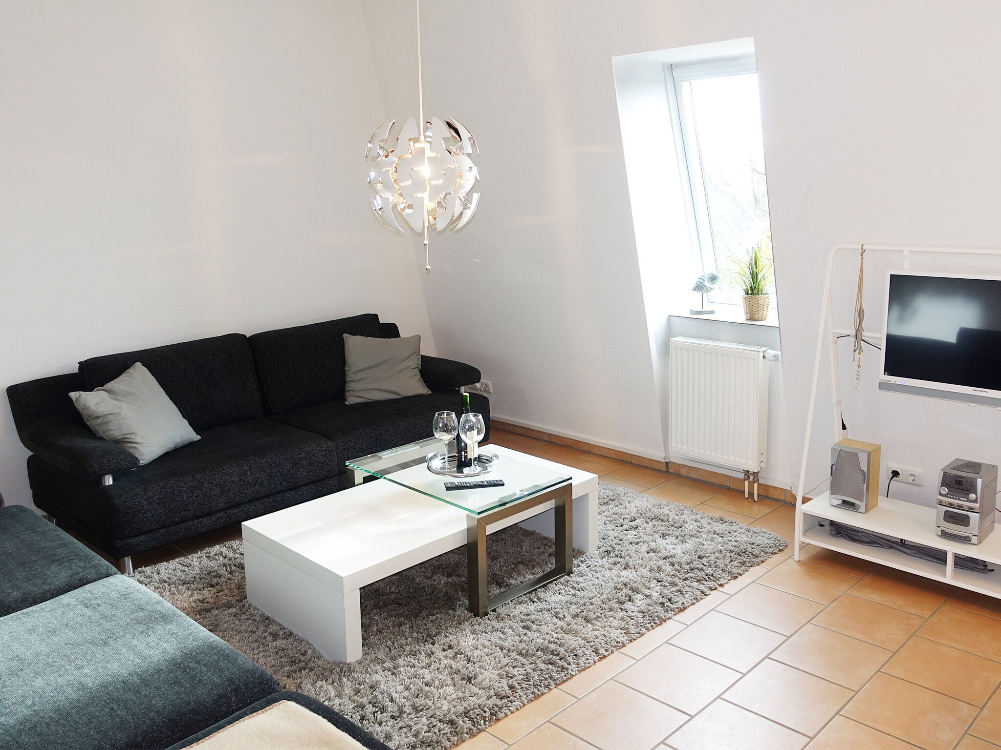 A modern living room with a black sofa, a white coffee table, and a glass-top table with wine glasses.