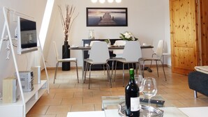 A modern living room with a dining area, a TV mounted on a stand, a wooden door, and a large window. - Intercontinental Family Home - North American Mediterranean Vacation Rentals (Hasselberg)