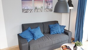 A modern living room with a grey sofa, blue cushions, a round coffee table with a book, a bottle of wine, and a small plant. - Intercontinental Family Home - North American Mediterranean Vacation Rentals (Hasselberg)
