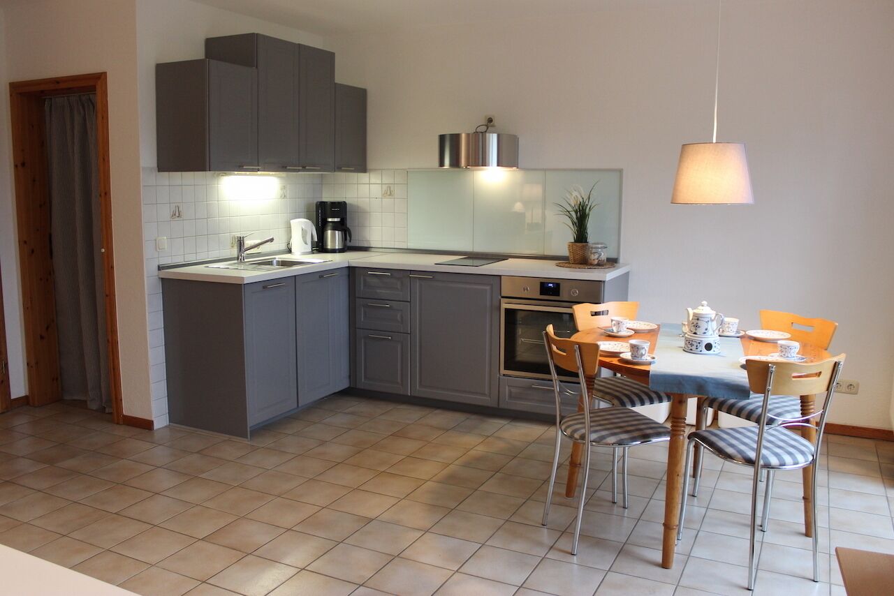 Eine moderne Küche mit grauen Schränken, einem eingebauten Backofen und einem Essbereich mit Tisch und Stühlen.