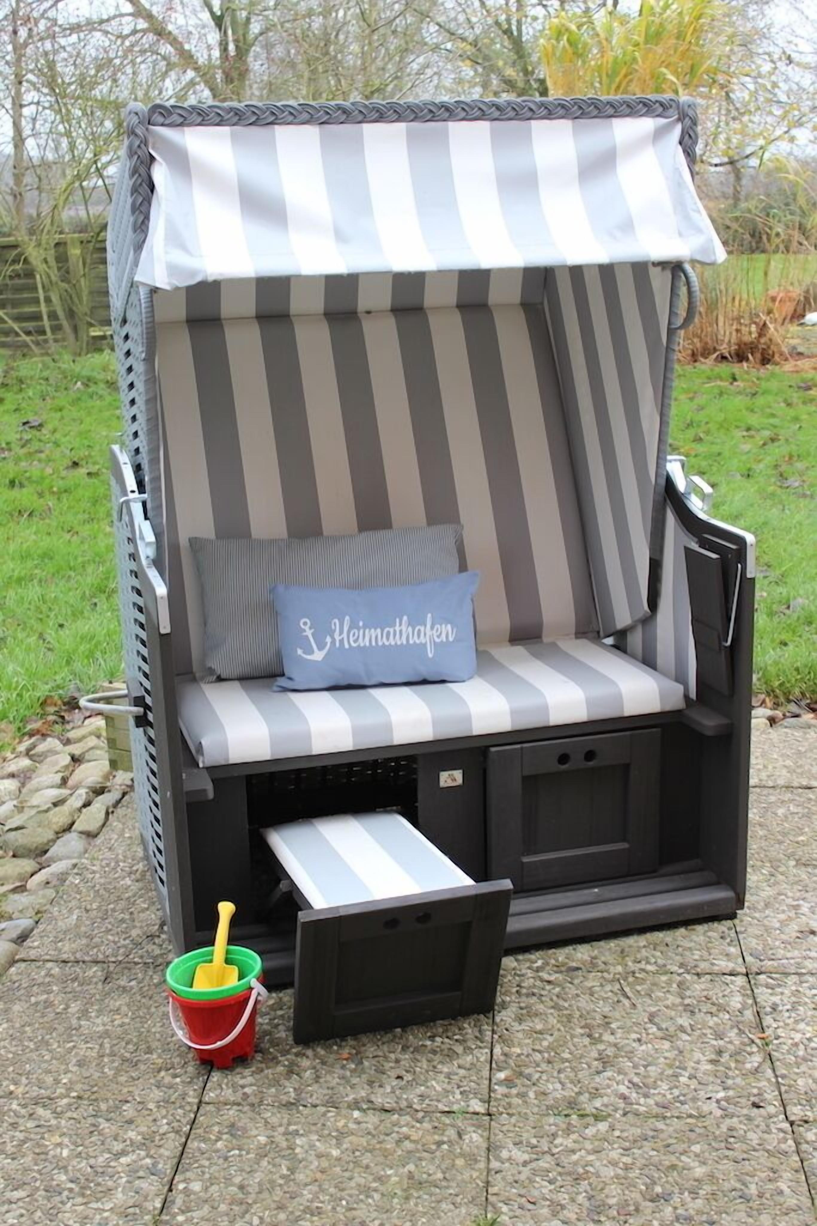 A striped outdoor lounge chair with a canopy, a cushion with a name, and a small red bucket with a yellow paddle.
