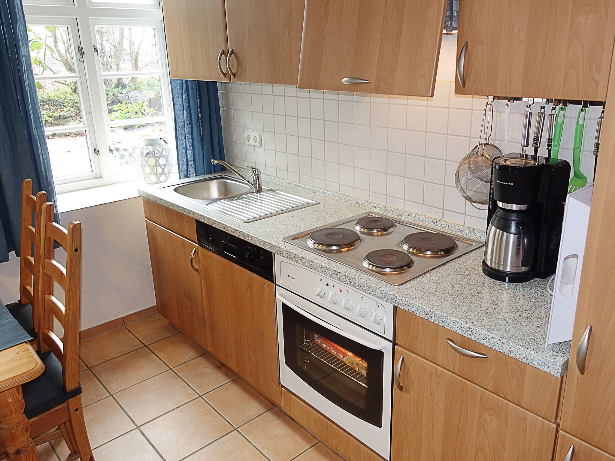 A kitchen with wooden cabinets, a stainless steel sink, a stove, an oven, and a coffee maker.