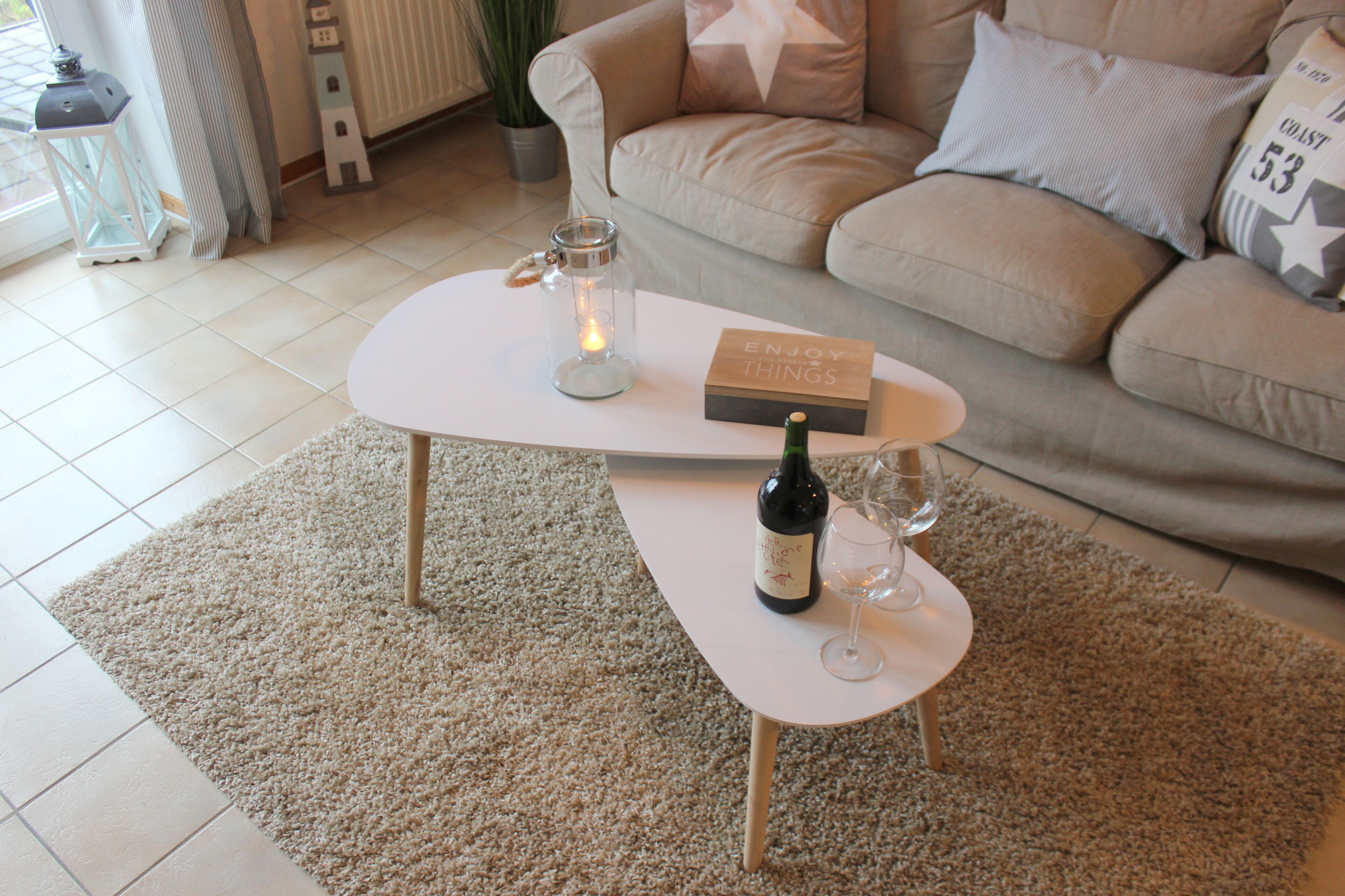 A cozy living room with a white coffee table, a candle, a wine bottle, and a glass.