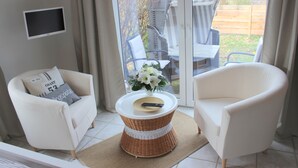 A room with a white armchair, a white sofa, and a wicker coffee table with a remote control on it. - Intercontinental Family Home - North American Mediterranean Vacation Rentals (Hasselberg)