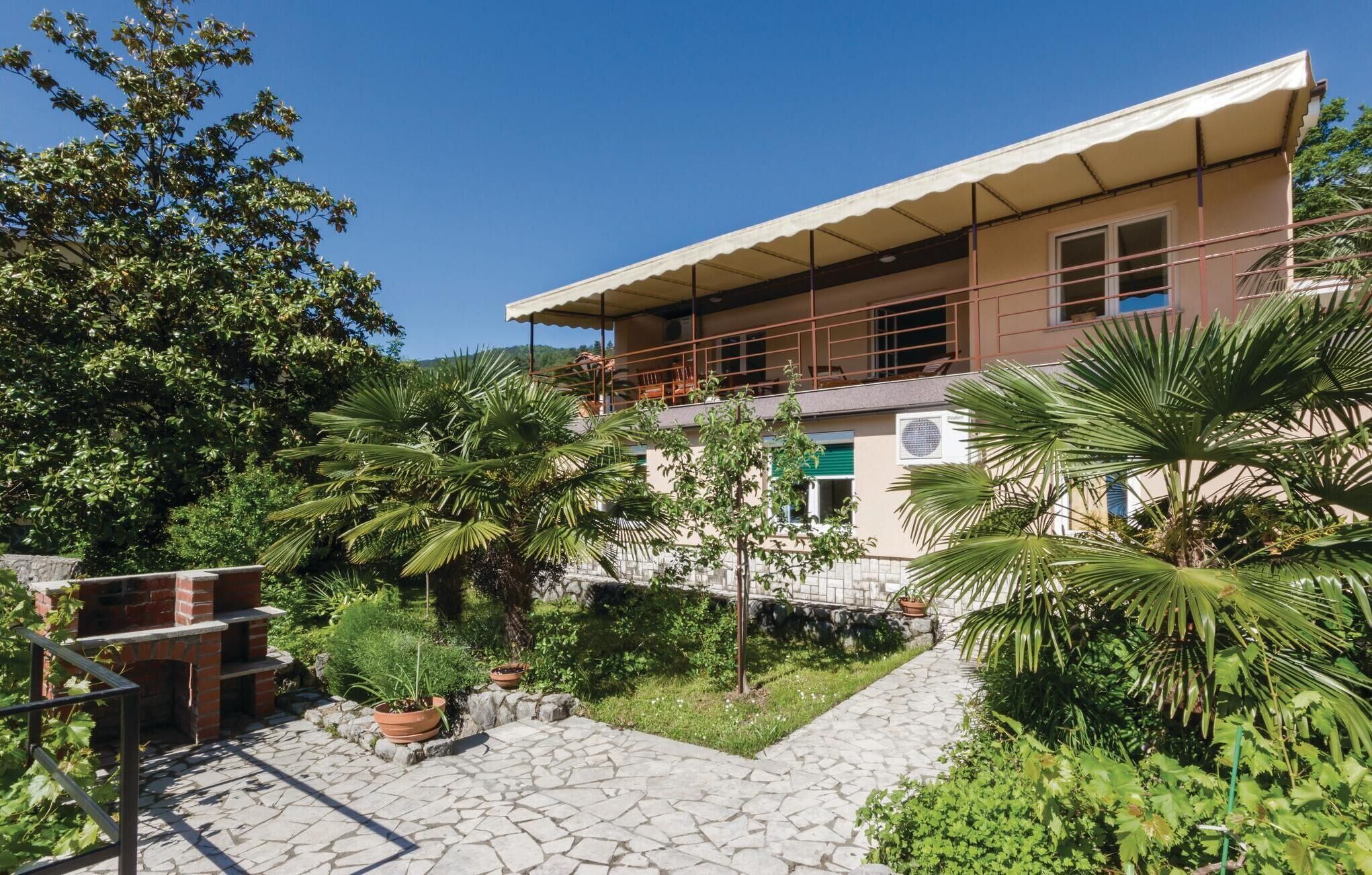 A two-story building with a balcony, surrounded by lush greenery and a stone pathway.