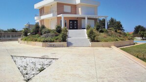 A modern two-story house with a flat roof, a balcony on the upper floor, and a front entrance with a set of stairs.