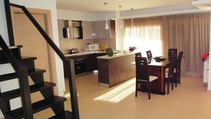 A modern kitchen with a central island, a dining area with chairs, and a staircase.