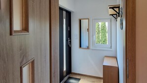 A hallway with a wooden door, a black door, a window with a view of greenery, and a small wooden bench. - 2 bedroom lovely home in Podamirowo (Podamirowo)