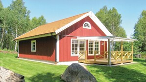 En röd trästuga med ett vitt tak, en veranda och en stor sten i förgrunden.