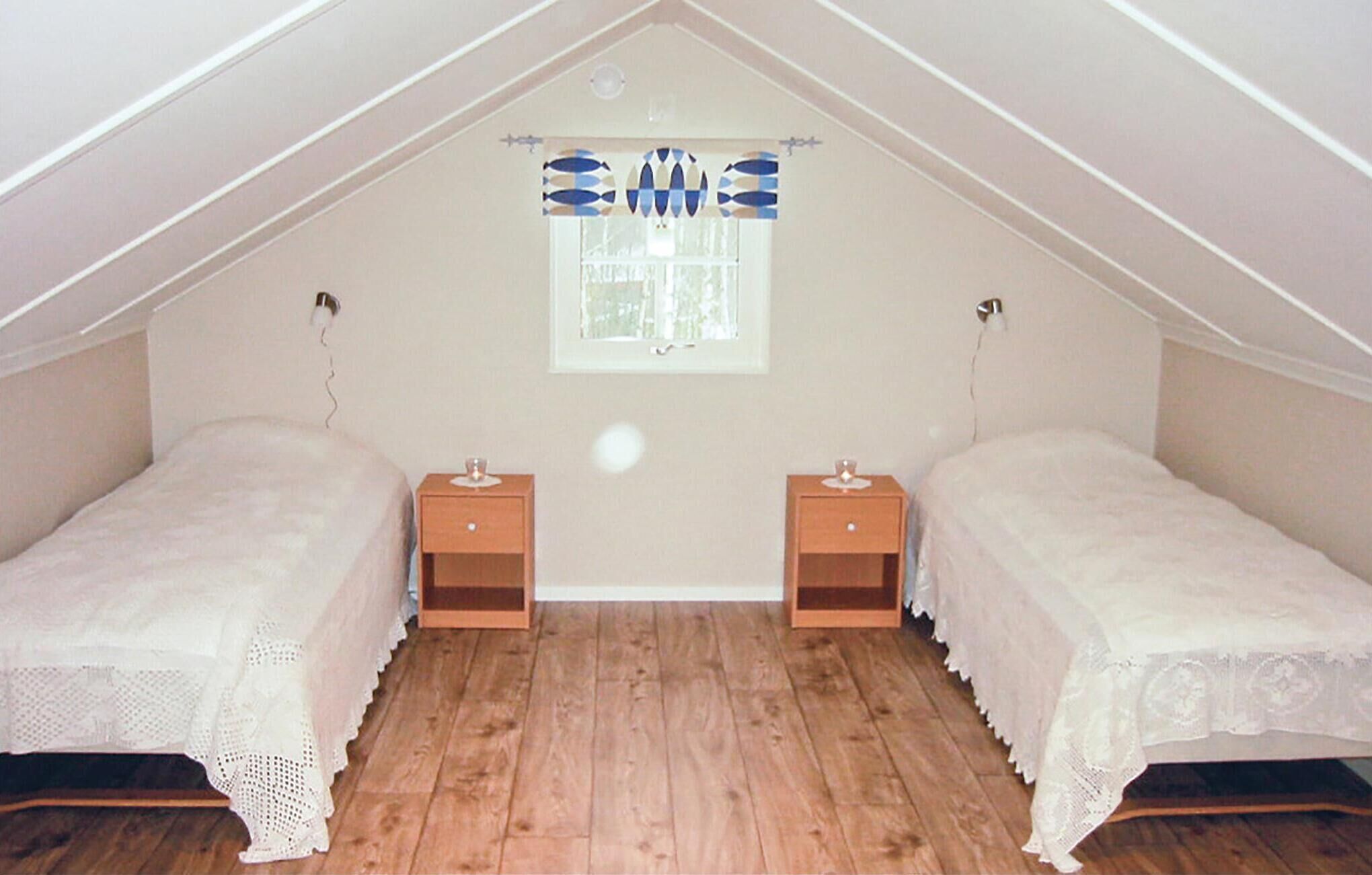 Un dormitorio acogedor en el ático, con dos camas individuales, mesitas de noche de madera y un ventanal con un diseño decorativo azul y blanco.