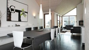 Ein moderner Essbereich mit einem langen Tisch, weißen Stühlen und Pendelleuchten.