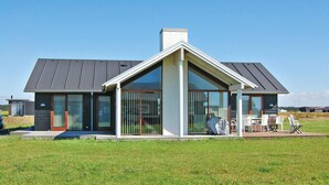 Ein modernes Haus mit einer großen Glasfassade, einem markanten, dreieckigen Dach und einem großzügigen Außenbereich mit Sitzgelegenheit.