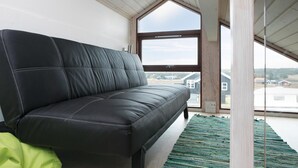 Ein schwarzes Ledersofa in einem Raum mit einem großen Fenster, einer Holzbalkendecke und einem grünen Teppich.