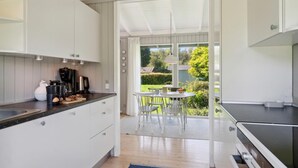 A modern kitchen with white cabinets, a black countertop, and a dining area with a table and chairs. - Amazing home in Tisvildeleje with WiFi (Tisvildeleje)