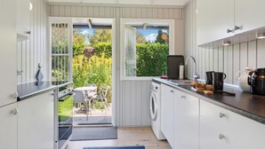 A compact kitchen with a washing machine, a sink, and a window overlooking a garden. - Amazing home in Tisvildeleje with WiFi (Tisvildeleje)
