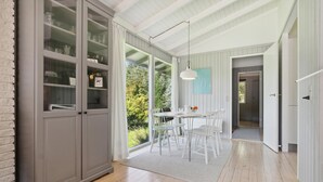 A modern kitchen with white cabinets, a dining area with a round table and chairs, and a view of greenery outside. - Amazing home in Tisvildeleje with WiFi (Tisvildeleje)