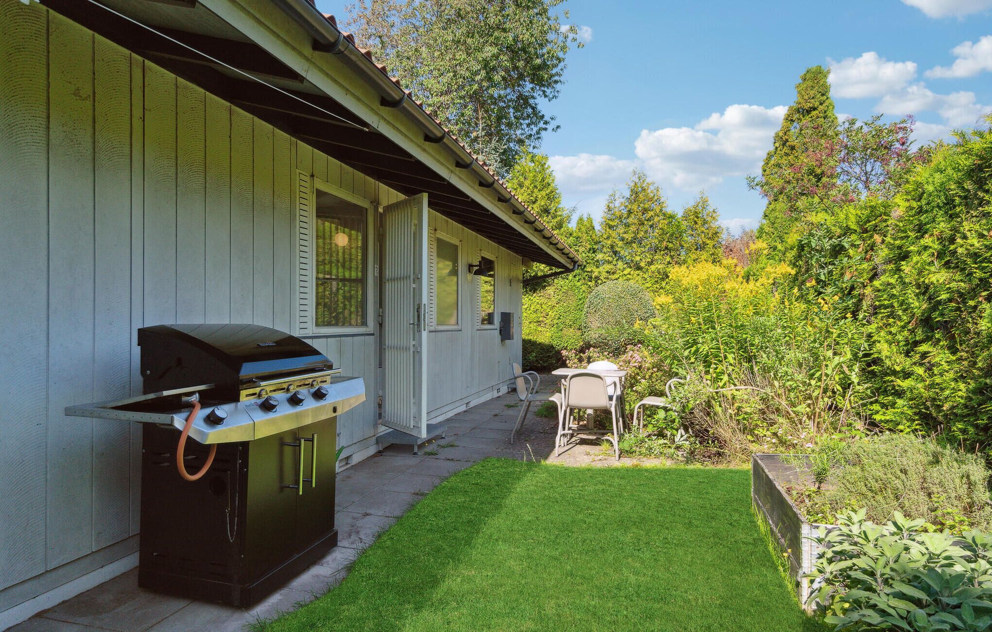 A backyard with a barbecue grill, a small patio table, and a lawn.