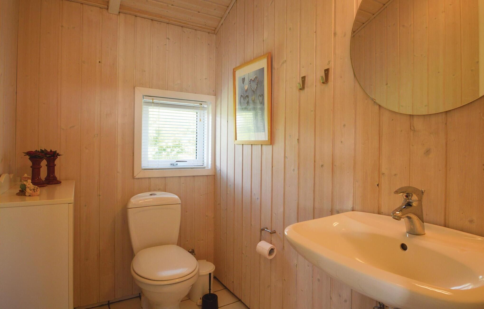 A small, wooden-paneled bathroom with a toilet, a sink, a window, and a framed picture on the wall.