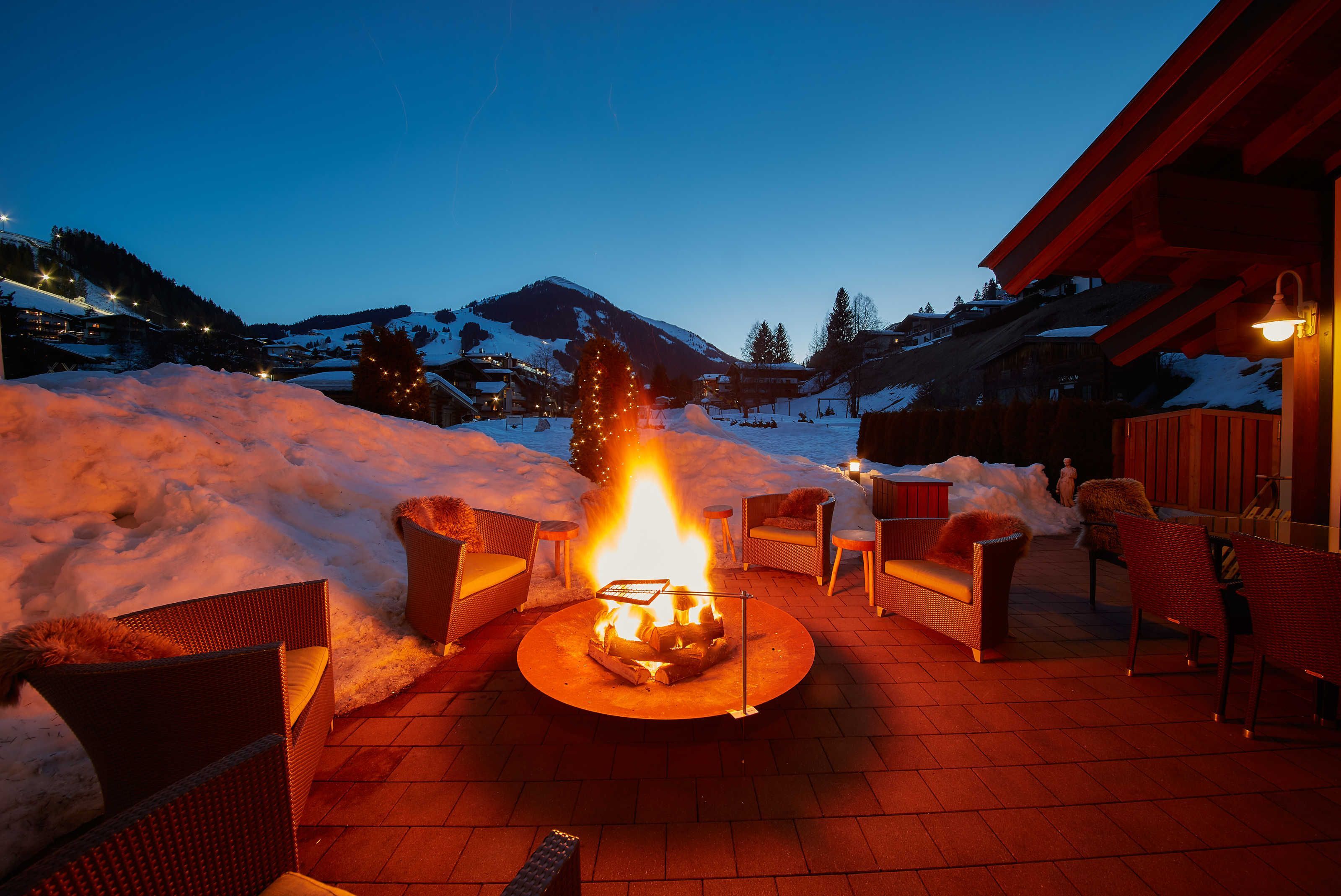 A fire pit with chairs, snow, and a mountain in the background.