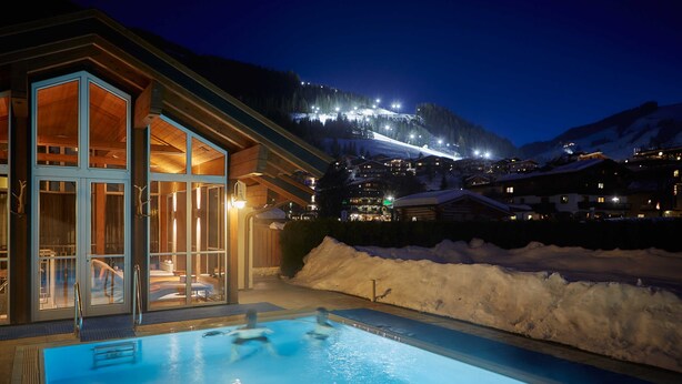 Ein Hotel mit Pool, Glastüren und Blick auf einen schneebedeckten Berg bei Nacht.