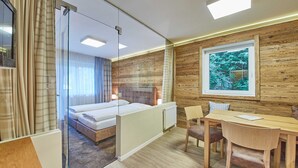 Ein modernes Hotelzimmer mit Glasabtrennung, einem Bett, einer Holzwand, einem Fenster mit Ausblick und einer Essecke.